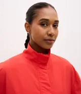 Campera deportiva de cuello alto con diseño color blocking en rojo y blanco. Presenta cierre frontal parcial, mangas largas con puños elásticos y bordado decorativo en el pecho. Confeccionada en poliamida con tecnología dry para mayor transpirabilidad.