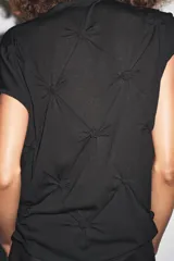 Top negro de manga corta y cuello subido, con detalle de nudos y frunces distribuidos en el frente y laterales, creando textura.