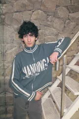 Campera de tejido de punto color verde petróleo, con cuello alto, cierre frontal completo y diseño deportivo con franjas laterales blancas en las mangas. Presenta el logo de la marca estampado en el frente.