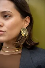 Aros colgantes hechos a mano en bronce dorado con forma irregular y bordes texturizados. Cada pieza es única.