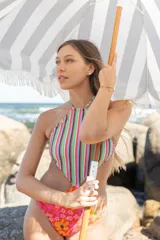 Trikini con diseño combinado, presentando un top de cuello halter con estampado de rayas verticales multicolores y una bombacha con estampado floral en tonos naranjas y rosas. La prenda cuenta con espalda descubierta y tiras ajustables.