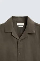 Camisa de lino color negro con calce relajado, cuello bowling y manga corta. Presenta cierre frontal con botones a tono y aberturas laterales en el bajo.