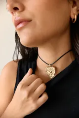 Collar con dije de corazón en acero quirúrgico, con textura irregular y relieve, montado sobre un tiento encerado negro.