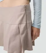 Short pollera de tiro alto en color beige, con diseño de sastrería, tablas delanteras y ruedo asimétrico.