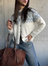 Cardigan de tejido de punto con diseño jacquard en la parte superior, cuello redondo y cierre frontal con botones. Presenta un patrón geométrico en tonos gris y azul sobre base color crema.