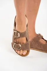 Sandalias marrones de cuero con dos tiras anchas ajustables con hebillas doradas. La plantilla es de corcho y la suela es de goma.