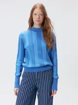 Sweater de punto con diseño de rayas verticales en tonos negro y gris oscuro. Presenta cuello alto tipo polera, mangas largas con puños ajustados y ruedo elástico. Incluye un pequeño bordado en color rojo en el pecho.