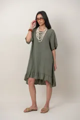Vestido midi de lino color beige, con mangas cortas, cuello redondo, alforzas verticales en el pecho y detalle de volados en el ruedo.