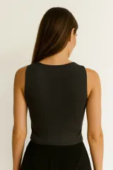 Top sin mangas color blanco hueso, de tejido acanalado, corte ajustado al cuerpo y cuello redondo con tres recortes en forma de ojo de cerradura en el centro del pecho.