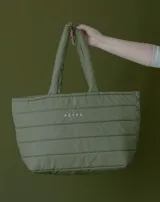 Bolso tipo tote de material impermeable y diseño acolchado con costuras horizontales, en color verde militar. Cuenta con doble asa superior y el nombre de la marca impreso en el frente.