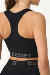 Top deportivo negro con logo blanco en el frente y banda elástica con letras grises en el bajo busto.