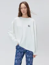 Remera oversize de manga larga blanca con cuello redondo y costuras visibles en contraste. Presenta un pequeño gráfico estampado de un sol en el pecho y diseño estampado en la espalda.