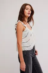 Musculosa blanca de poliéster con diseño romántico, tirantes con volados, detalles de encaje y cierre frontal con cordón ajustable y botones.