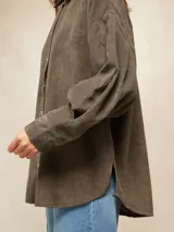 Camisa de pana color oliva, con corte oversize, cuello clásico, cierre frontal con botones metálicos y mangas largas con puños abotonados.