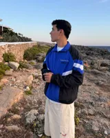 Campera deportiva de diseño colorblock en tonos azul, negro y blanco, con cierre frontal y cuello alto. Presenta detalles de franjas y un pequeño estampado en el pecho con la inscripción "Uruguay Run Club".