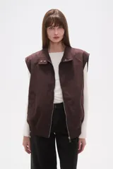 Chaleco marrón oscuro con cuello alto, cierre frontal de cremallera plateada y puños y bajo elásticos.