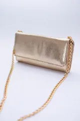Cartera tipo sobre color beige con textura granulada y correa de cadena dorada.