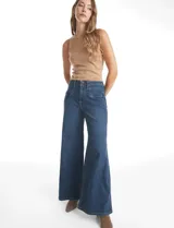 Jean de tiro alto con corte wide leg, confeccionado en denim azul. Presenta cierre frontal con botón, pasacintos y bolsillos delanteros aplicados con pespuntes decorativos.