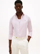 Camisa de hombre Tommy Hilfiger de manga larga a rayas verticales rosas y blancas, confeccionada en algodón regenerativo elástico. Tiene corte slim fit, cuello clásico, cierre con botones, puños abotonados y logo bordado en el pecho.