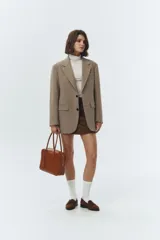 Blazer de lana color beige, con solapas de cuello sastre, cierre frontal de dos botones y bolsillos rectangulares. Presenta un calce relajado tipo overfit y hombreras marcadas.
