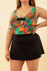 Vestido de baño enterizo con estampado de hojas, piñas y animal print. Tiene escote con abertura en forma de gota y moño negro. La parte inferior es una falda negra.