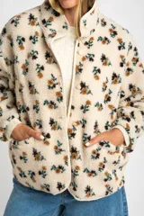 Campera de corderito con estampado floral, cuello alto y cierre frontal con botones a presión. Posee puños elásticos y un diseño de ajuste al cuerpo.