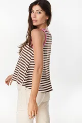 Musculosa de corte holgado con diseño a rayas horizontales en tonos marrón y crudo. Presenta ribetes en color fucsia en el cuello redondo y en las sisas, además de un pequeño bordado decorativo en el centro del pecho.