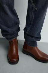 Bota de piel color marrón con cierre de cremallera lateral, horma cuadrada y suela con ligero tacón.