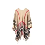 Poncho abierto de tejido de punto con diseño de cuadros escoceses en tonos beige, negro, blanco y detalles en rojo. Presenta terminaciones con flecos en el ruedo.