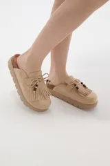 Suecos tipo mocasín color chocolate, confeccionados en material gamuzado. Presentan un diseño con flecos frontales, cordones decorativos con cuentas y una suela de plataforma plana de goma.