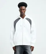 Saco con capucha y cierre frontal de cremallera, confeccionado en tejido de algodón y poliéster. Presenta un diseño bicolor con cuerpo blanco y paneles laterales en gris oscuro, mangas largas y bolsillos delanteros.