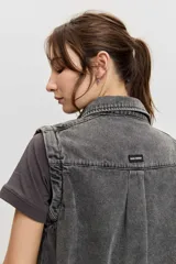 Chaleco de denim color gris deslavado, con cuello camisero, cierre frontal con botones metálicos y costuras decorativas.