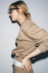 Sudadera de algodón color beige, con cuello redondo, manga larga y corte ligeramente corto. Presenta un pequeño parche cuadrado marrón con un logo grabado en el pecho.