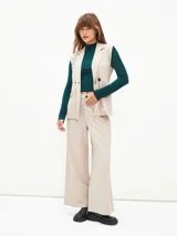 Chaleco beige con solapas, doble botonadura, lazo para atar en la cintura y bolsillos delanteros.