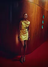 Vestido corto de satén color amarillo, con diseño sin mangas, cuello redondo y detalle de fruncido y nudo en el hombro. Presenta un corte recto y espalda abierta.