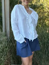 Camisa de lino color gris claro, de manga larga y corte holgado, con cuello mao y detalle de volados en el frente a lo largo de la botonera.