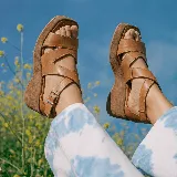Sandalias de cuero color suela, con plataforma y taco alto de madera forrado, tiras cruzadas en el empeine y tira ajustable con hebilla en el talón.