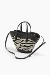 Cartera tipo tote con diseño de estampado animal print de cebra, confeccionada en tejido jacquard con detalles en material sintético negro. Cuenta con doble asa de mano, correa larga ajustable y extraíble para usar como bandolera, y cierre interno de mosquetón.