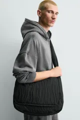 Bolso de hombro confeccionado en tejido técnico acolchado de color negro. Presenta un diseño de solapa con cierre magnético y cremallera, asa de hombro integrada y compartimentos interiores.