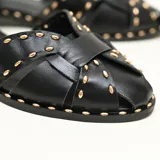 Sandalias chatitas color negro de cuero 100% natural, con diseño de tiras cruzadas en el empeine, pulsera al tobillo con hebilla metálica dorada y apliques de tachas doradas alrededor de las tiras y la suela.