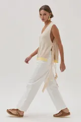 Chaleco tejido de algodón color beige, con escote en V, lazos laterales y terminaciones con pompones.