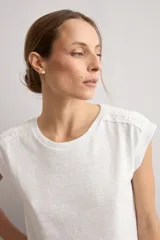 Remera mostaza de manga corta con detalles de encaje bordado (broderie) en los hombros, cuello redondo y corte recto.