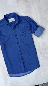 Camisa de jean azul con cuello italiano, manga larga con puños enrollados y dos bolsillos frontales con solapa.