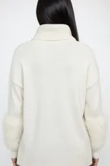 Polerón de cuello alto en color crudo, confeccionado en tejido de punto con mangas largas que presentan puños de textura afelpada y diseño holgado.