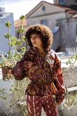 Campera impermeable con capucha y cierre frontal, con estampado de hojas en tonos marrones y ocres. Tiene bolsillos laterales ocultos y cordón ajustable en la cintura.