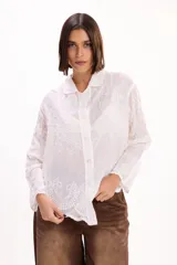 Camisa blanca de manga larga con cuello clásico y cierre frontal de botones. Presenta un delicado diseño bordado floral en toda la prenda con detalles calados.