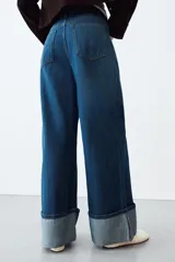 Jeans de tiro alto con corte wide leg, confeccionados en denim azul. Presentan diseño de cinco bolsillos, cierre frontal con cremallera y botón, y bajo con vuelta ancha.