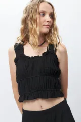 Top negro sin mangas, elastizado y texturizado, con breteles anchos y volados en el escote y ruedo.