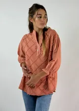Blusa color beige con cuello mao, mangas 3/4 con puños elásticos y detalle de diseño geométrico texturizado en el frente.