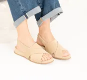 Sandalias de gamuza color avena, con diseño de tiras cruzadas en el empeine, talón destalonado con elástico interno para mayor sujeción y suela plana con leve plataforma.